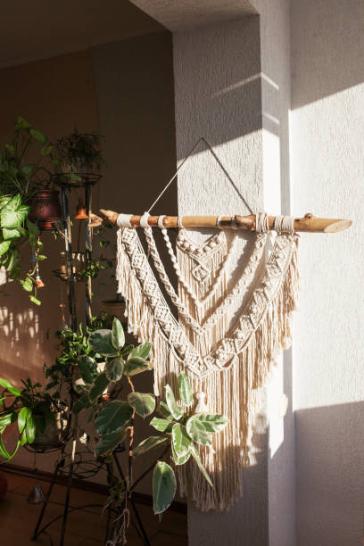 istock Handmade macrame  100% cotton wall hanging with green leafes on a white wall.  Modern eco macrame decoration with wooden stick in the interior. Bright solar light 1305259366