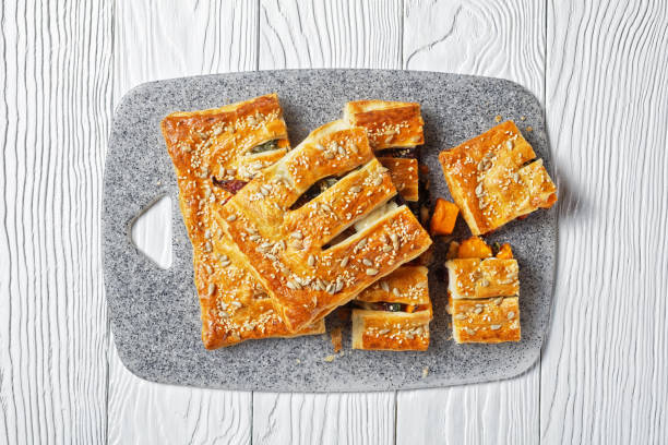 tarte américaine de pâte feuilletée de légumes avec le fromage de chèvre garni de graines de tournesol et de sésame remplies de légumes rôtis servis sur un fond en bois blanc, vue supérieure, plan rapproché - puff pastry pumpkin garlic cheese photos et images de collection