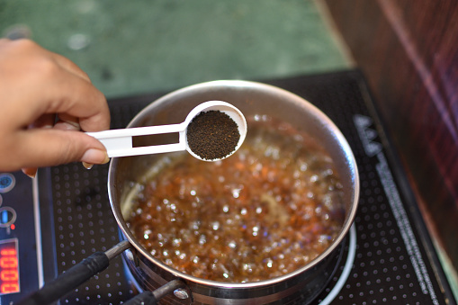 adding black tea leaves and a pinch of herb mixture to boiling water with grated ginger, for preparing the black, herbal tea at home. Selective focus