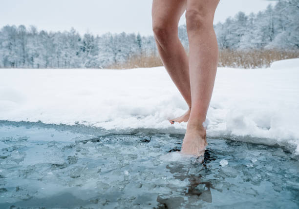 primo passo delle gambe femminili che entrano nell'acqua ghiacciata - fare il bagno foto e immagini stock