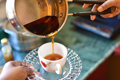 Close up of a woman's hand pouring herself a mug of hot black harbal tea from a steel pot.