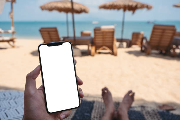 istock a man holding mobile phone with blank desktop screen while sitting on the beach 1305265216