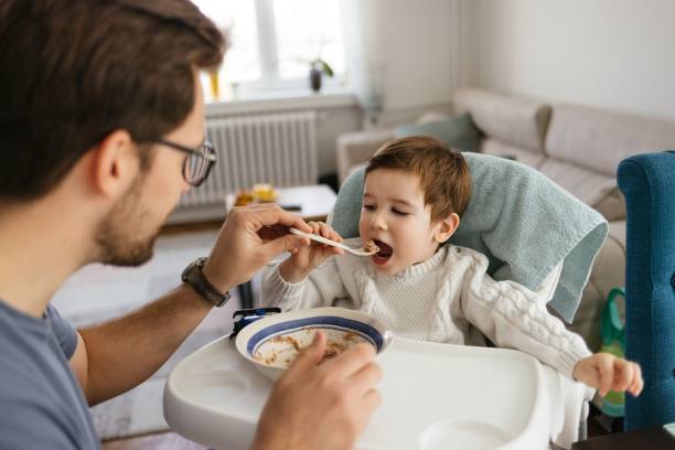 istock Caring single father spoon feeding his beautiful son 1305268243