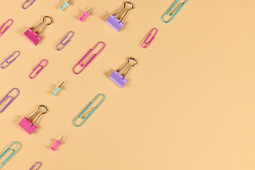 Stationery items like paper clips and drawing pins arranged on side of yellow background with empty copy space