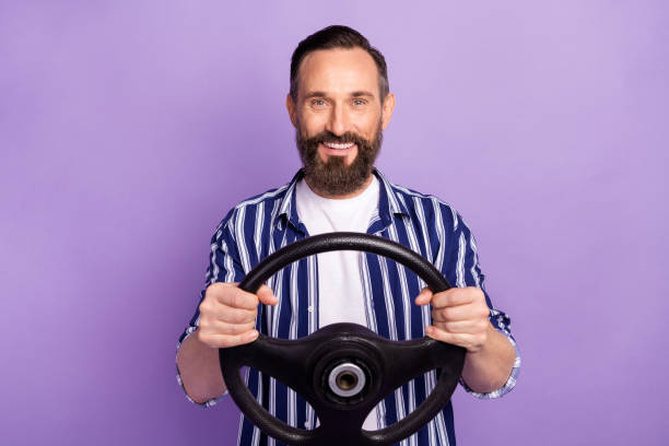 foto dell'uomo maturo conducente tenere il volante isolato su sfondo di colore viola - steering wheel foto e immagini stock