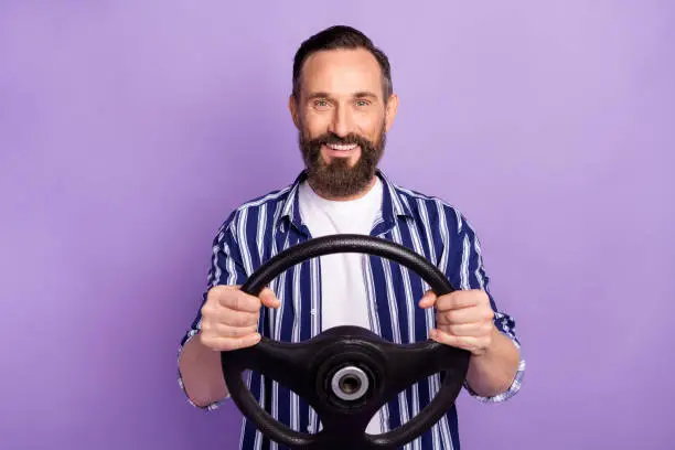 Photo of mature man driver hold steering wheel isolated over purple color background.