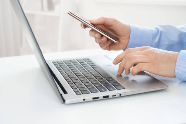 istock Woman hands with smartphone using laptop at workplace or home 1305270930