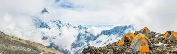 Mountaineering tents overlooked by the iconic pyramid peak of Machapuchare (6993m) high in the Himalayan mountain wilderness of the Annapurna Conservation Area, Nepal.