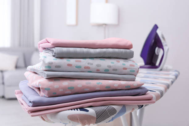 istock Stack of clean bed linens on ironing board in room 1305272047