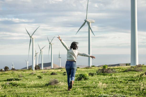 mujer irreconocible corriendo en prado con molinos de viento - run of the mill fotografías e imágenes de stock