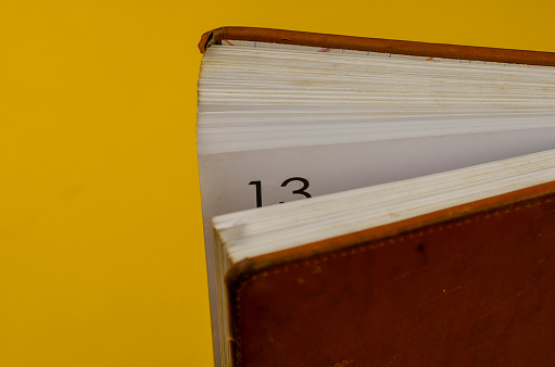 Close-up of an Old diary standing on the endpaper against a yellow background. Half-opened diary with the number 13 on a worn page.