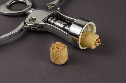 Old corkscrew and broken cork on a gray background. The corkscrew lies next to a broken wine cork. Selective focus