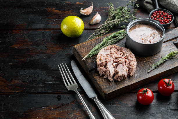 atún en lata, entero y picado, en tablero de corte de madera, sobre viejo fondo de mesa de madera oscura
 con hierbas e ingredientes, con espacio de copia y espacio para el texto - can packaging tuna food fotografías e imágenes de stock