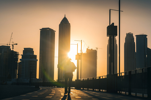 Woman having a sunset walk in downtown Dubai public walking promenade in Business Bay. Back-lit view of a urban lifestyle in a modern city