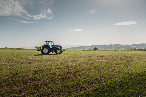 A tractor fertilizing a green field under a clear blue sky