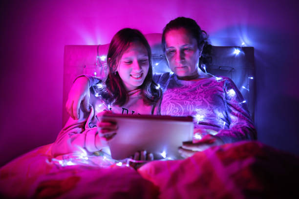 istock Mother and daughter watching video from tablet under LED light 1305284624