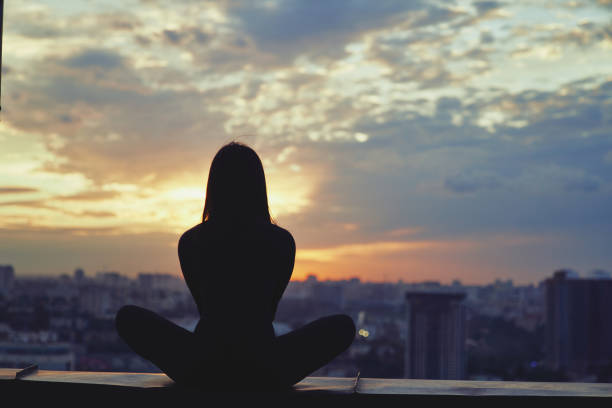 istock Woman practicing yoga at colorful sunset with urban view 1305284908