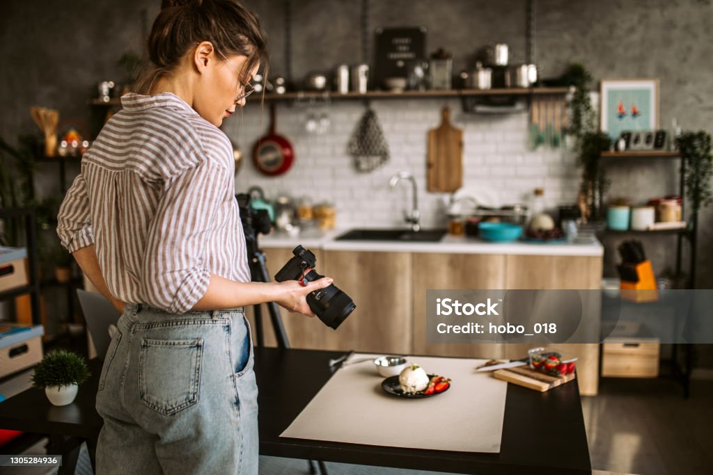 Photographer woman in her studio Young female photographer standing over food set, holding camera, photographing different types of food ingredients Rear View Stock Photo