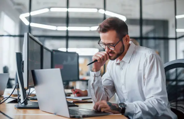 Male stockbroker in formal clothes works in the office with financial market.