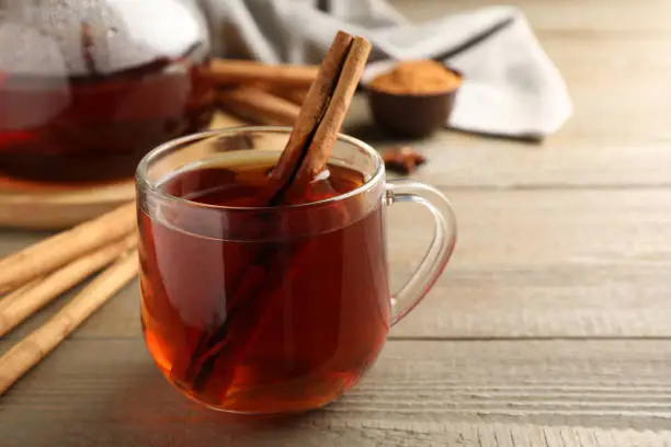 Glass cup of hot tea with aromatic cinnamon on wooden table. Space for text