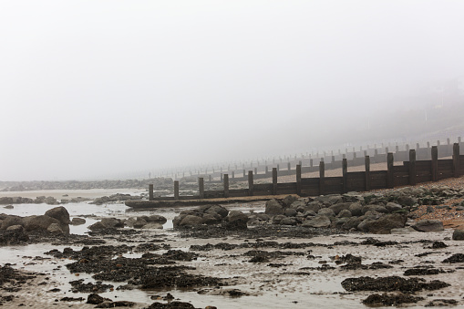 Wooden gutters on a pebbly beach on the Eastbourne coast on a foggy day