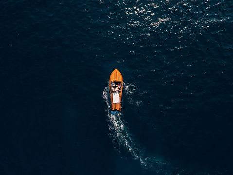 A wooden sports boat with people on board rides on the sea. Luxury wooden motor boat - top view from drone. High quality photo
