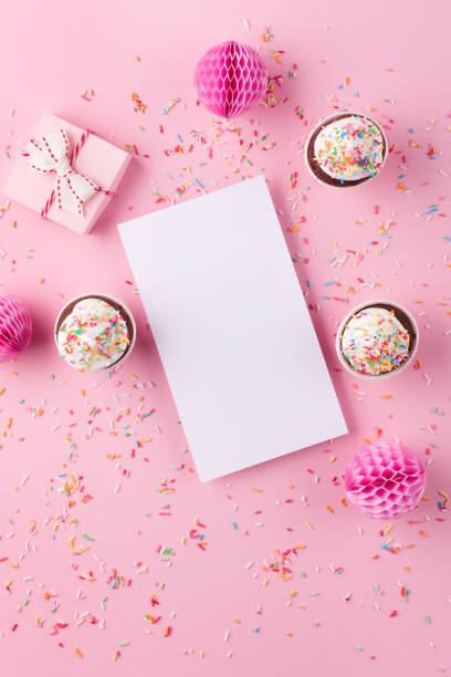 istock Empty white blank, gift box, paper decorations and cupcakes on pink sprinkles background. 1305291177