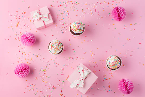 istock Festive gift boxes, pink paper decorations, sweet macaroons and cupcakes on pink sprinkles background. 1305291185