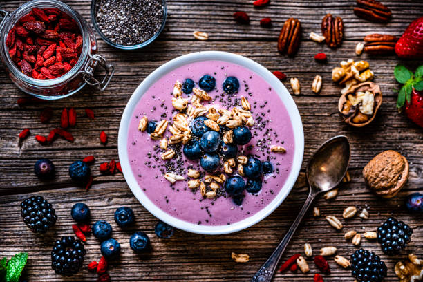 Mixed berries smoothie bowl on rustic wooden table. Healthy eating: overhead view of a mixed berries smoothie bowl with oat, chia seeds and nuts shot on rustic wooden table. Blackberries, blueberries, goji berries, pecan, walnuts and chia seeds are around the smoothie bowl. High resolution 42Mp studio digital capture taken with Sony A7rII and Sony FE 90mm f2.8 macro G OSS lens smoothie stock pictures, royalty-free photos & images