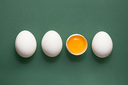 Four White eggs, yolk on green pastel background. Copy space. Minimal concept.