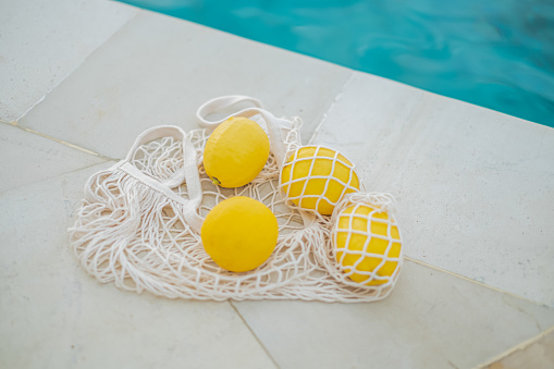 Flatlay shot of lemons in an eco-friendly mesh bag at the poolside.