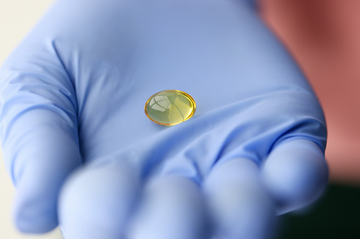 Yellow capsule of vitamin D lying on doctors hand closeup. Preventive vitamin intake concept