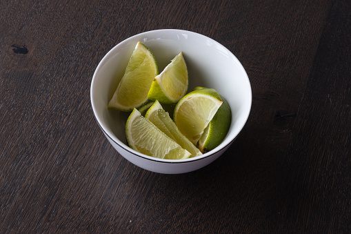 Fresh sliced lime wedges inside of a white bowl on a wooden table