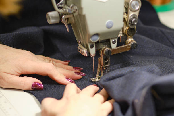 istock Female hands stitching white fabric on professional manufacturing machine at workplace. Close up view of sewing process. Light blurred background 1305306560