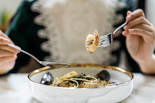 Image of an Asian Chinese woman having a plate of seafood cream pasta in restaurant