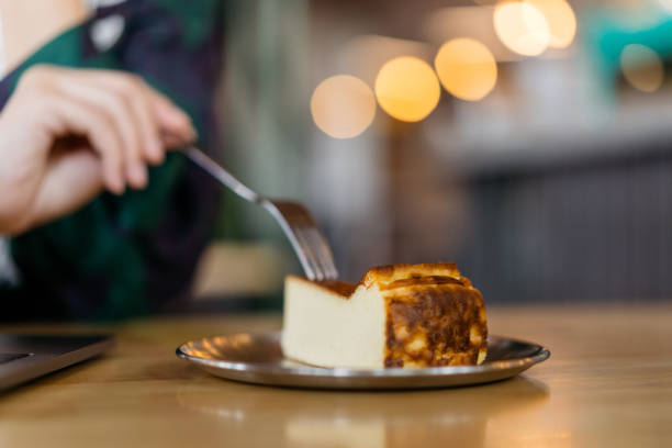 Close up of hand of an Asian Chinese woman using laptop while having a slice of cheesecake in a cafe