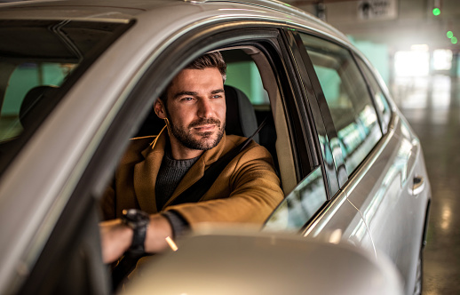 Photo of happy mid adult man driving a car in public garage.