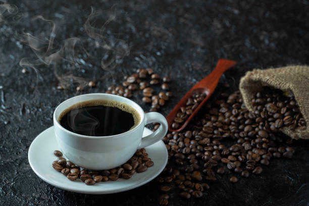 istock Hot black coffee with smoke for morning beverage menu in white ceramic cup with coffee beans roasted in burlap sack bag on dark grunge rustic table background. Flat lay with copy space. 1305312144