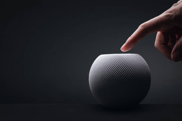 Apple HomePod mini with a hand on dark background A white HomePod mini from Apple photographed in a dark light setting. A hand with an outstretched finger is above the HomePod. Copy space to the left. virtual assistant stock pictures, royalty-free photos & images