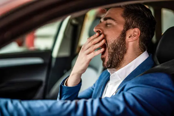 Tired mid adult businessman driving a car and yawning.