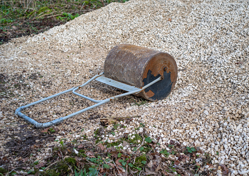 A heavy metal hand roller on a white gravel surface with slight rust.