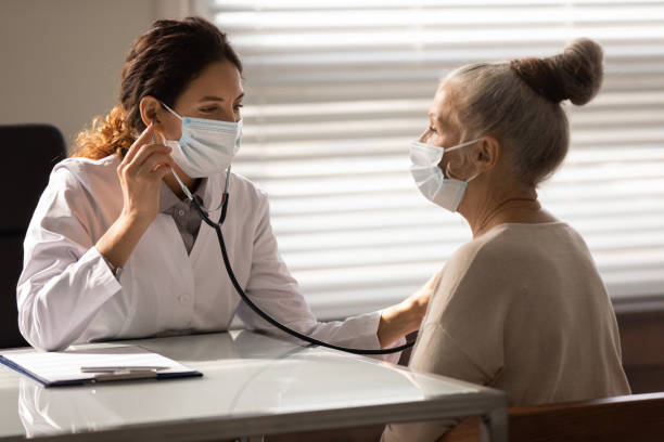 close up doctor wearing face mask checking mature patient lungs - ouvindo batidas do coração imagens e fotografias de stock