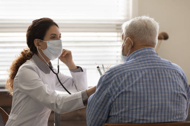 doctora que usa máscara facial revisa pulmones de hombre maduro - chest stethoscope medical exam men fotografías e imágenes de stock