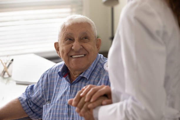 Close up smiling mature man and caregiver holding hands Close up smiling mature man and female caregiver wearing white uniform holding hands, doctor nurse comforting and supporting senior patient at meeting in hospital, expressing empathy and care alzheimers disease stock pictures, royalty-free photos & images