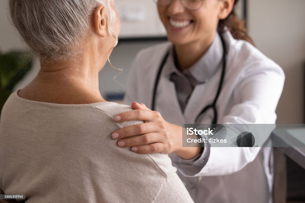 Close up back view smiling doctor touching mature patient shoulder Close up back view smiling female doctor wearing uniform touching mature patient shoulder, expressing empathy and care, successful treatment or medical checkup result, psychological help concept Patient Stock Photo