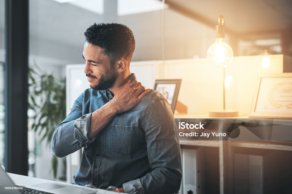 I've got a kink in my neck Cropped shot of a handsome young businessman sitting alone in the office at night and suffering from stiff muscles Organization Stock Photo