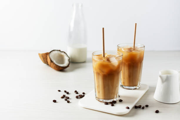 Iced coffee with coconut milk in a tall glass on white wooden table. Iced coffee with coconut milk in a tall glass on white wooden table. Cold refreshment summer drink. coconut milk stock pictures, royalty-free photos & images