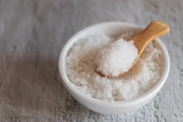 Flower of salt on wooden spoon in white bowl (Fleur de sel) is a salt that forms as a thin, delicate crust on the surface of seawater as it evaporates.