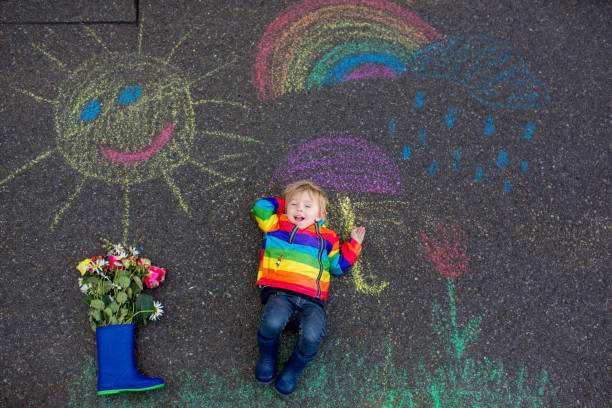 istock Cute toddler. playing in the rain with chalks, drawing on the asphalt, having fun 1305322496