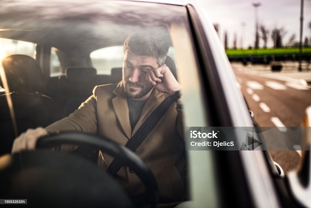 Man falling asleep while driving a car. Mid adult man falling a sleep while driving a car. Or having eye sight problems. Driving Stock Photo